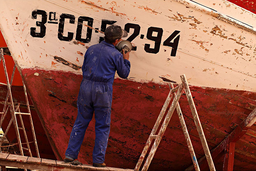 Un trabajador repara un barco de pesca en un dique.